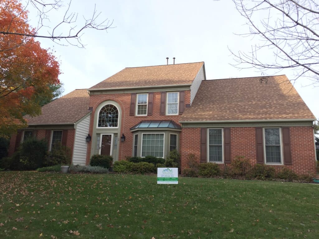 Brick townhouse with brown shutters under a multi-gabled roof, fall leaves on the lawn and a small sign in front yard advertising remodeling services.