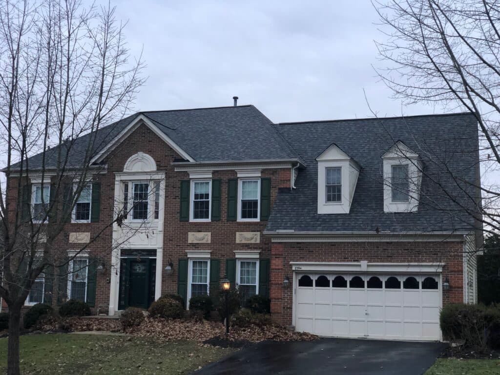 Brick townhouse with green shutters, white trim, and a large white garage door, set on a cloudy day with leafless trees in front.
