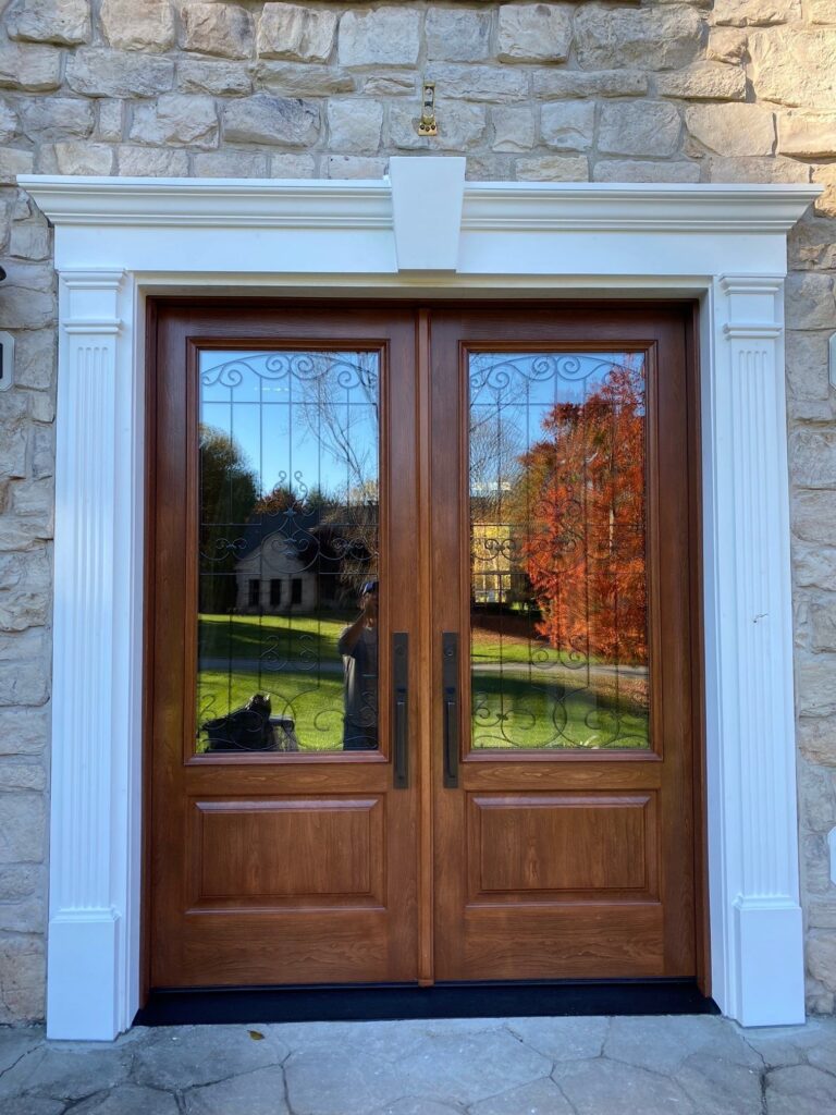 Double wooden front doors with decorative glass and wrought-iron grille, set in white classical door frame against a stone wall.